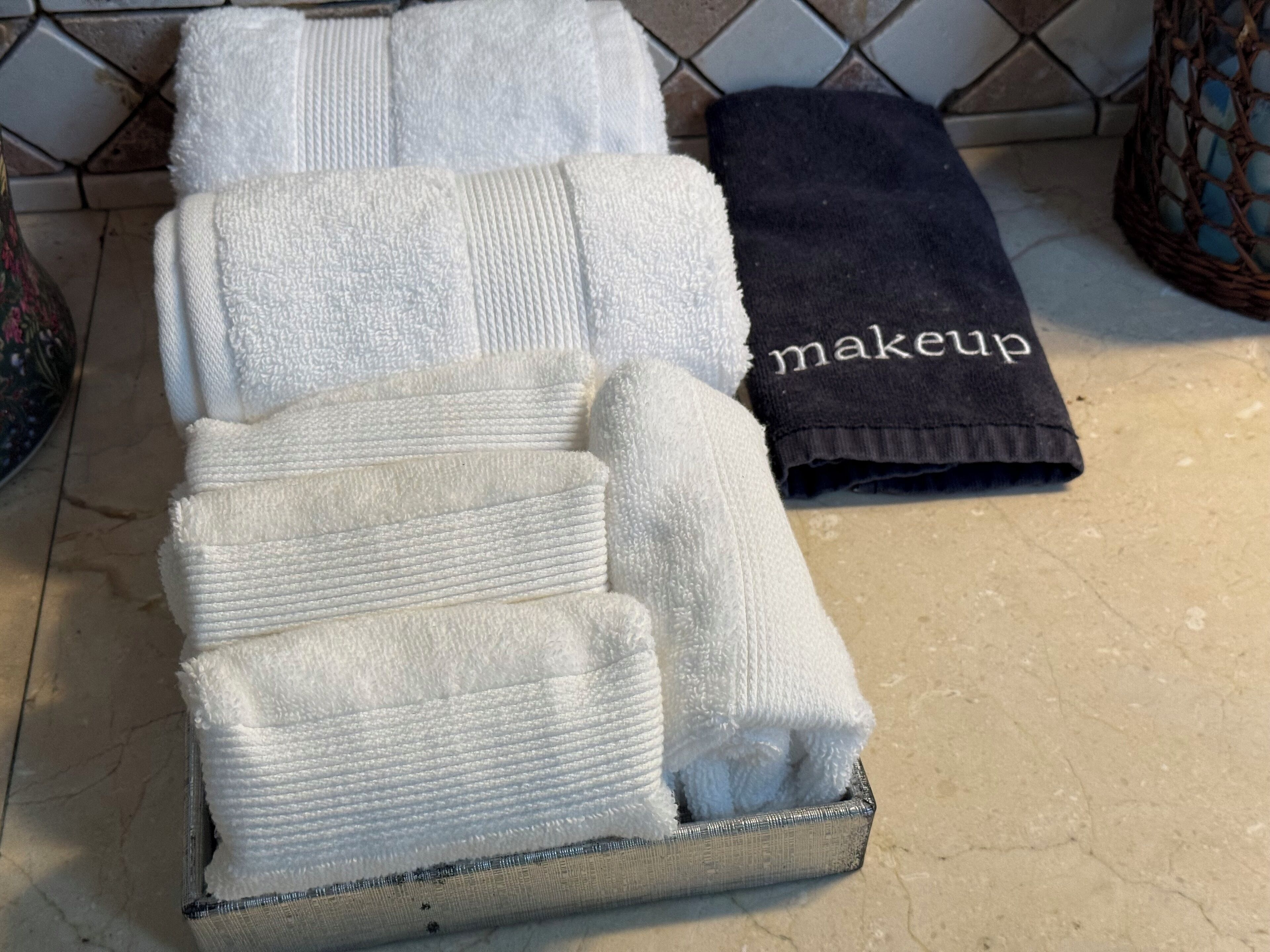Un juego de toallas dobladas con cuidado en una bandeja metálica, con una toalla etiquetada 'makeup'.