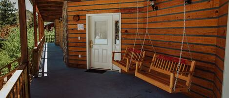 Une cabane en bois avec une véranda, une balançoire et une porte.
