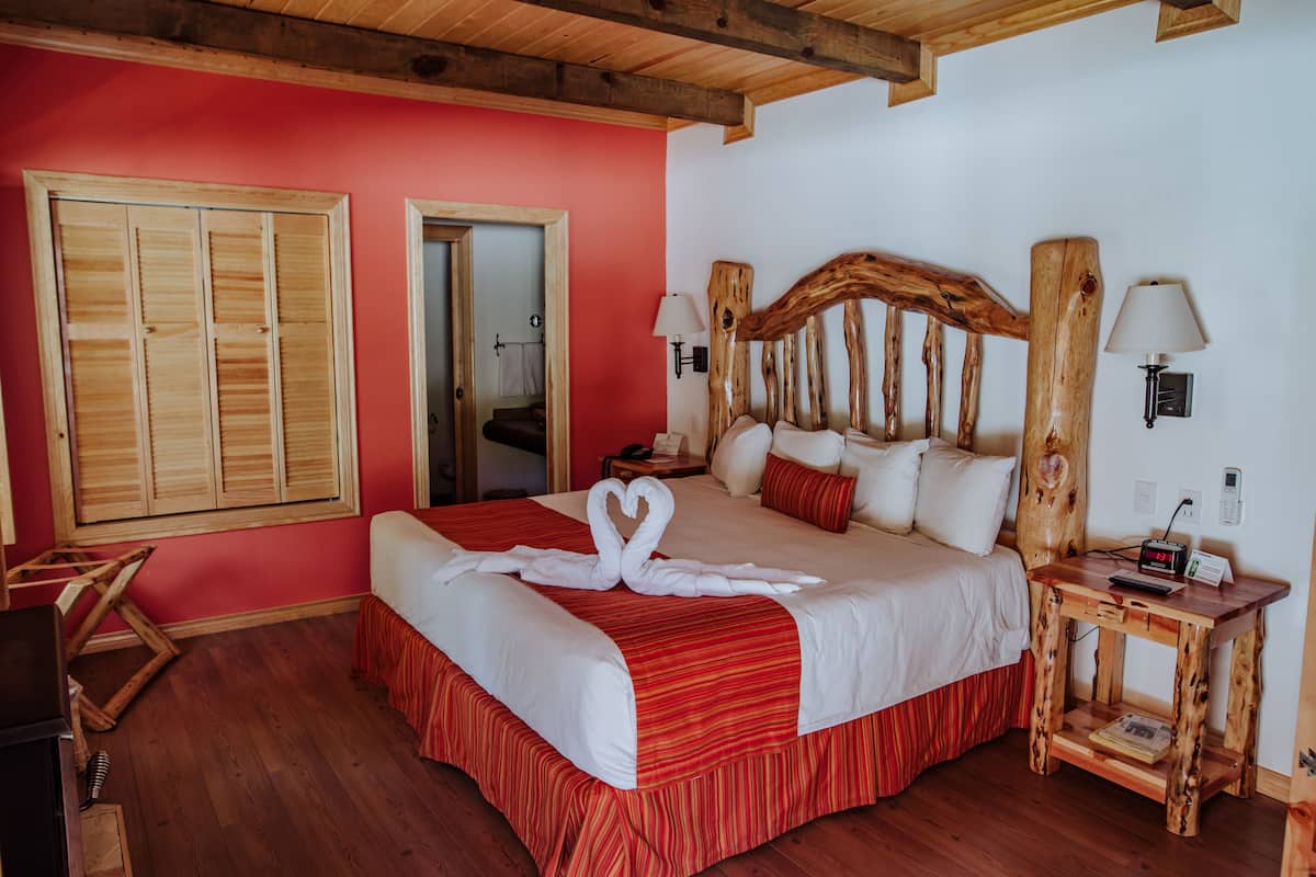 Une chambre d’hôtel avec un grand lit, une tête de lit en bois, des murs rouges et une table de chevet en bois avec une lampe.