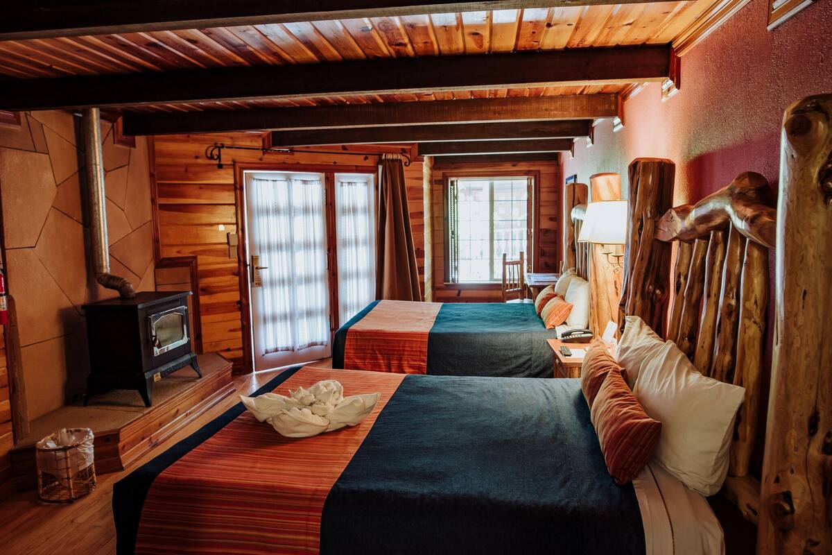Une pièce confortable avec deux lits, un poêle en bois et une fenêtre avec des rideaux.
