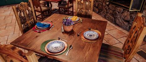 Una mesa de madera para comer dispuesta con platos, cubiertos y un jarrón de flores moradas.