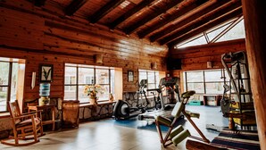 A spacious gym with wooden walls and large windows, featuring exercise equipment like treadmills and stationary bikes.