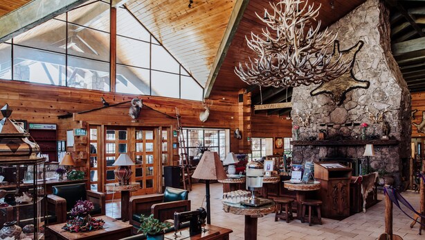 A rustic interior with wooden walls, a stone fireplace, and a variety of seating areas.