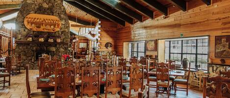 A rustic interior with wooden walls, a stone fireplace, and multiple wooden tables and chairs.
