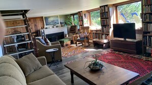 A cozy living room with a fireplace, comfortable seating, a television, and a bookshelf. - Wellfleet Harbor Waterfront-Duck Creek Cottage (Wellfleet)