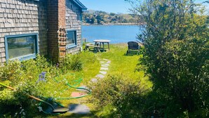 A house with a view of a lake, a garden with a lawnmower, and a picnic table. - Wellfleet Harbor Waterfront-Duck Creek Cottage (Wellfleet)