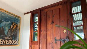 A wooden door with a metal latch, a framed picture on the wall, and a potted plant in the foreground. - Wellfleet Harbor Waterfront-Duck Creek Cottage (Wellfleet)