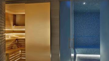 A modern bathroom with a glass shower enclosure, wooden shelving, and a visible tiled floor.