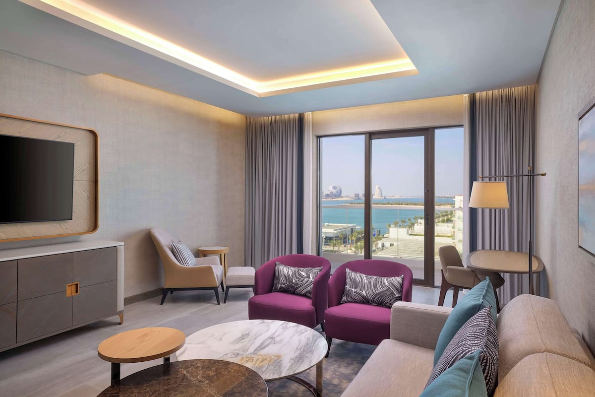 Ein modernes Hotelzimmer mit großem Fenster und Blick auf die Stadt, einem Flachbildfernseher und einer Sitzecke mit Sofa und Sesseln.