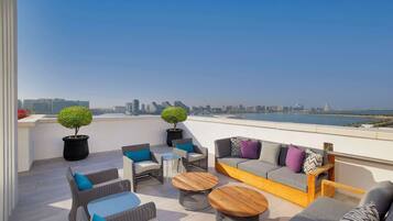 Eine Dachterrasse mit Korbmöbeln, runden Holztischen und Blumentöpfen.