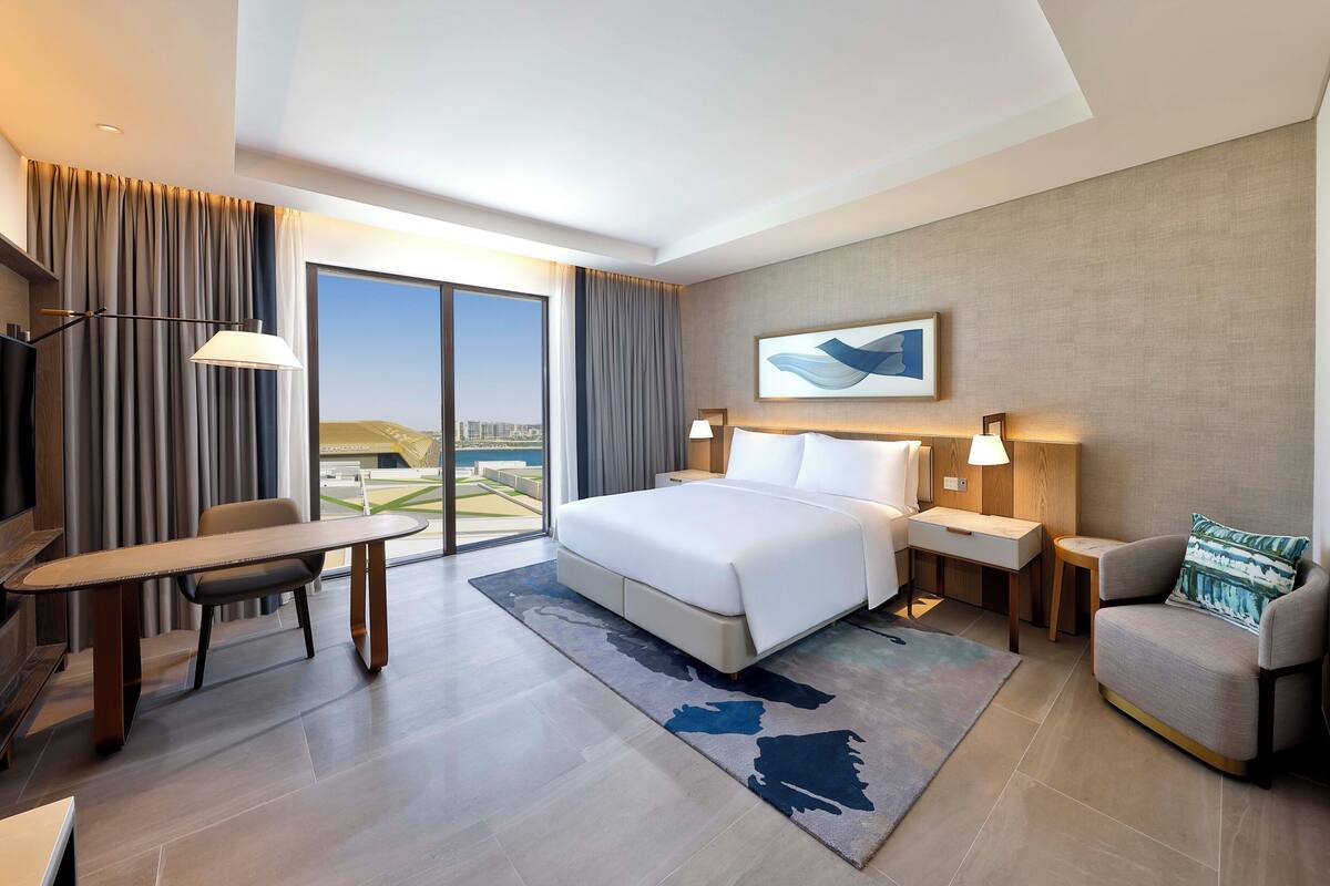 Ein modernes Hotelzimmer mit einem großen Bett, einem Schreibtisch, einem Stuhl und Blick auf die Stadt.