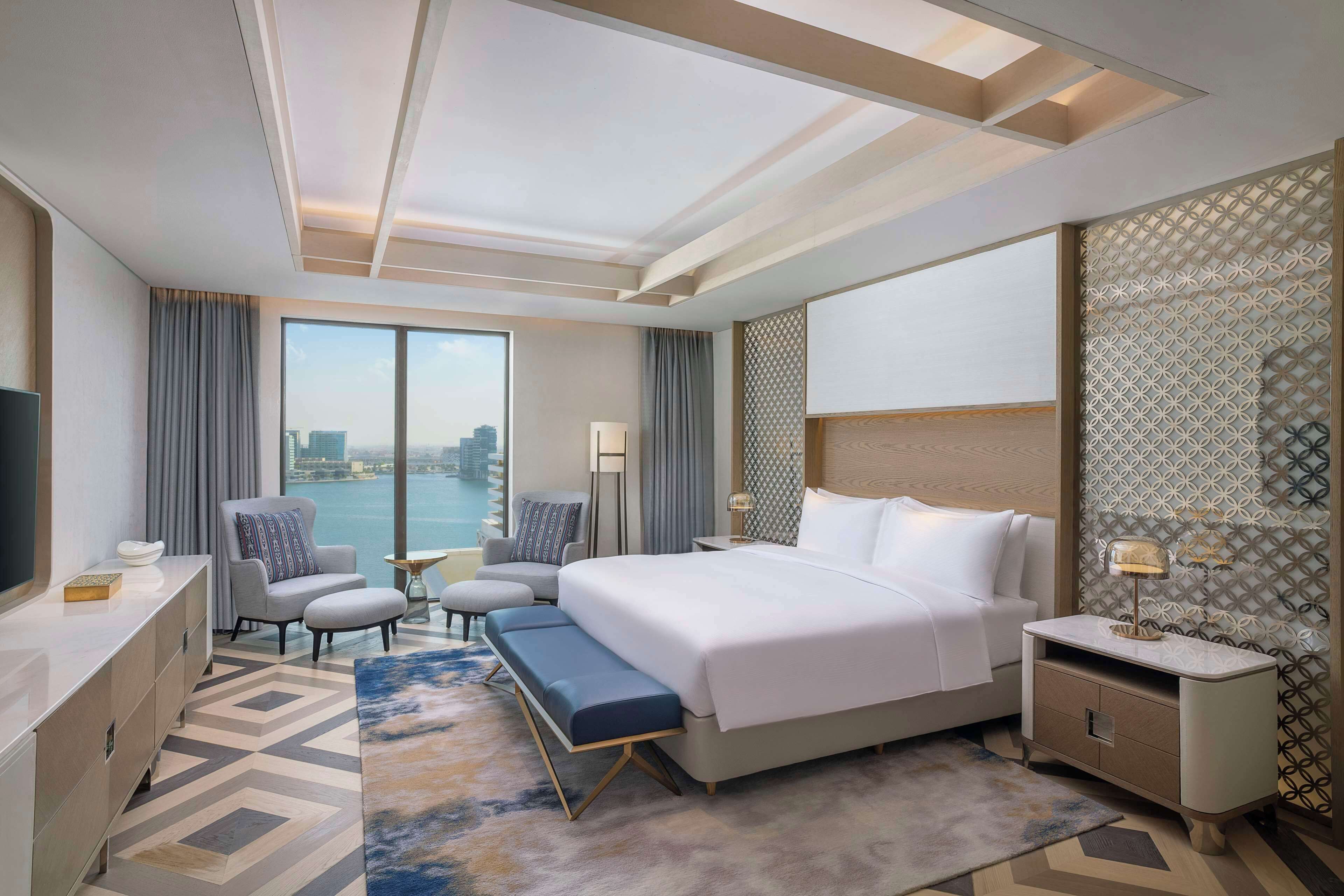 Ein modernes Hotelzimmer mit einem großen Bett, zwei Sesseln, einem Schreibtisch und Blick auf die Stadt.