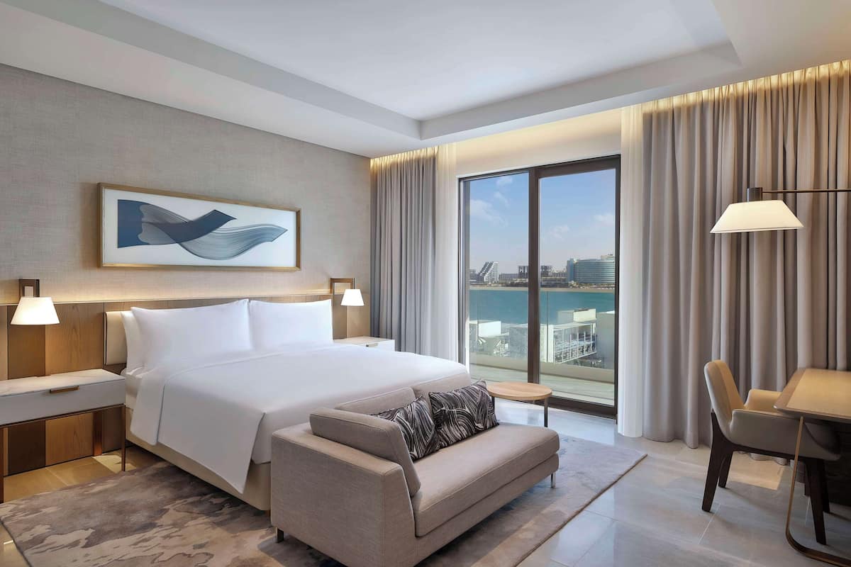 Ein modernes Hotelzimmer mit einem großen Bett, einer Sitzecke, einem Esstisch und Blick auf die Stadt.