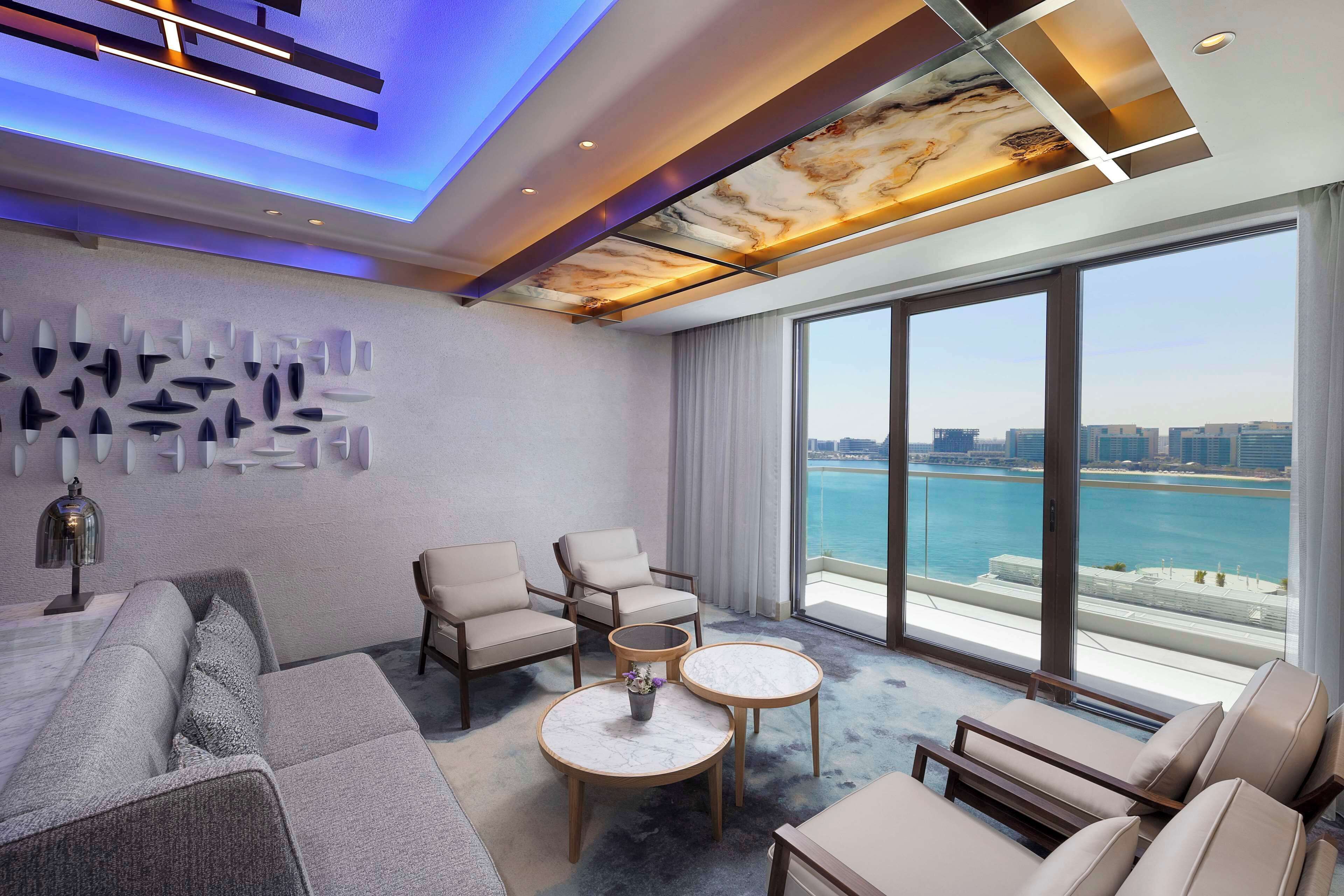 A modern hotel room with a large balcony, a city view, and a ceiling with a marble design.