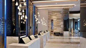 Een moderne hotellobby met marmeren receptiebalies, een zithoek en een decoratieve lichtinstallatie.