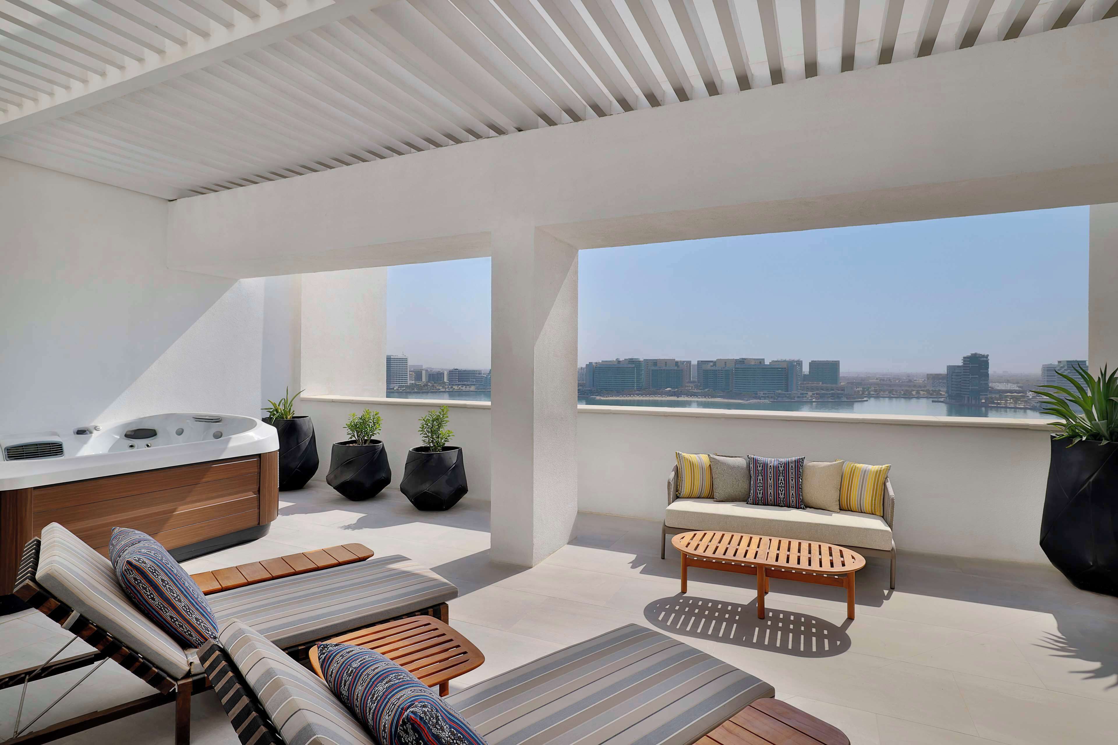 A rooftop terrace with a hot tub, lounge chairs, a sofa, and potted plants.