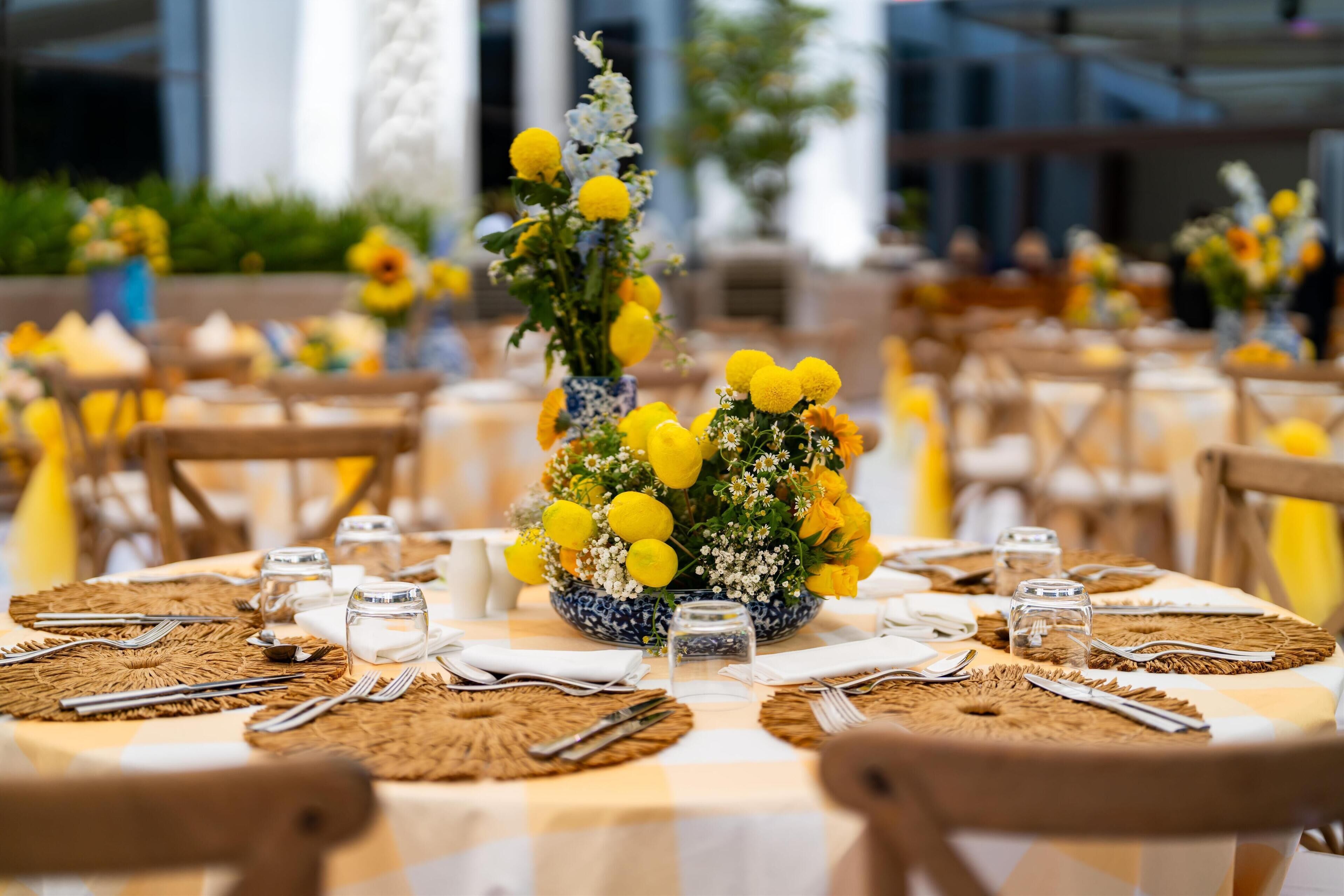 Een eetgedeelte met ronde tafels, versierd met gele bloemen, witte servetten en metalen bestek.