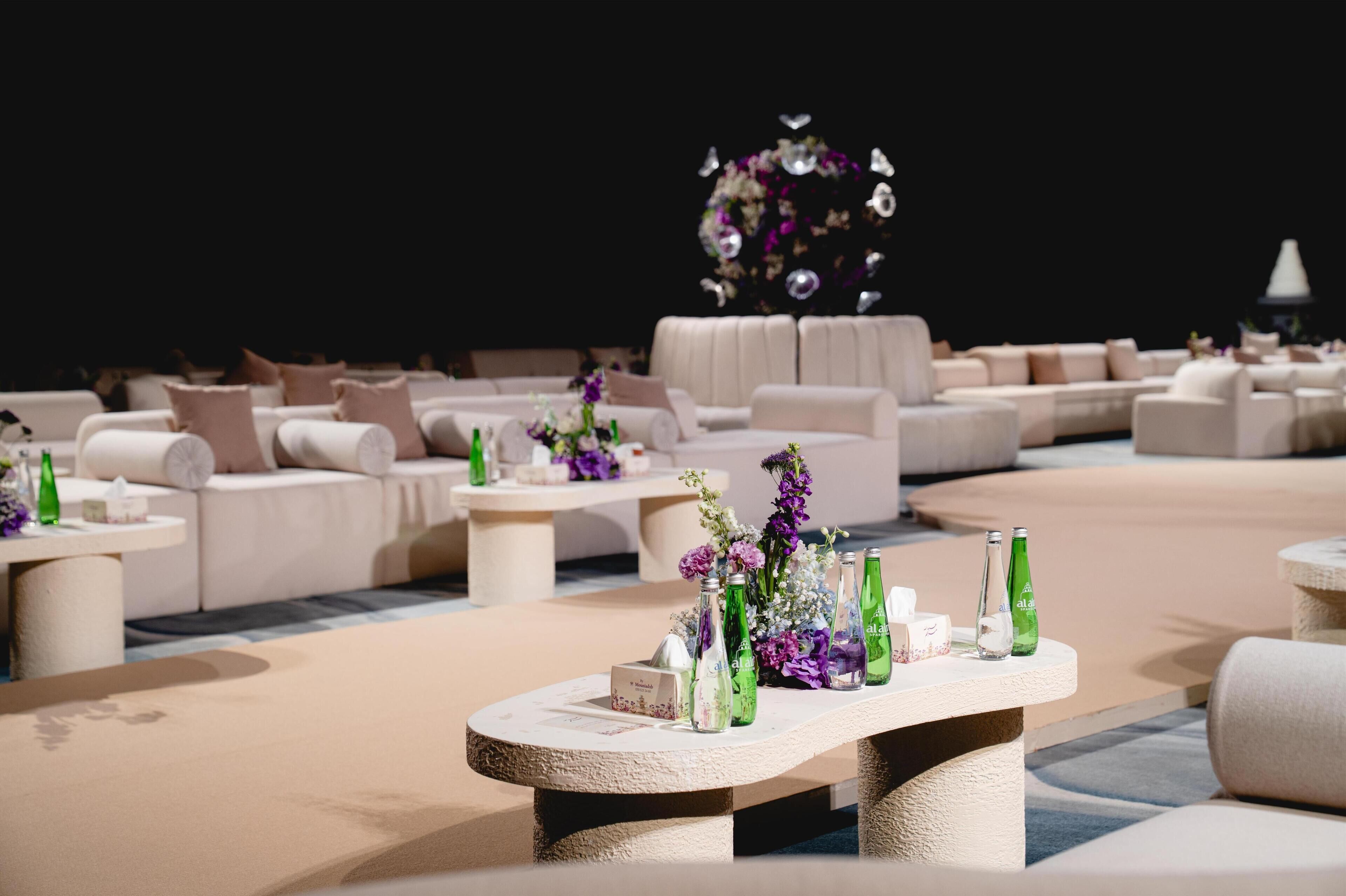 A modern lounge area with sofas, tables, and decorative floral arrangements.