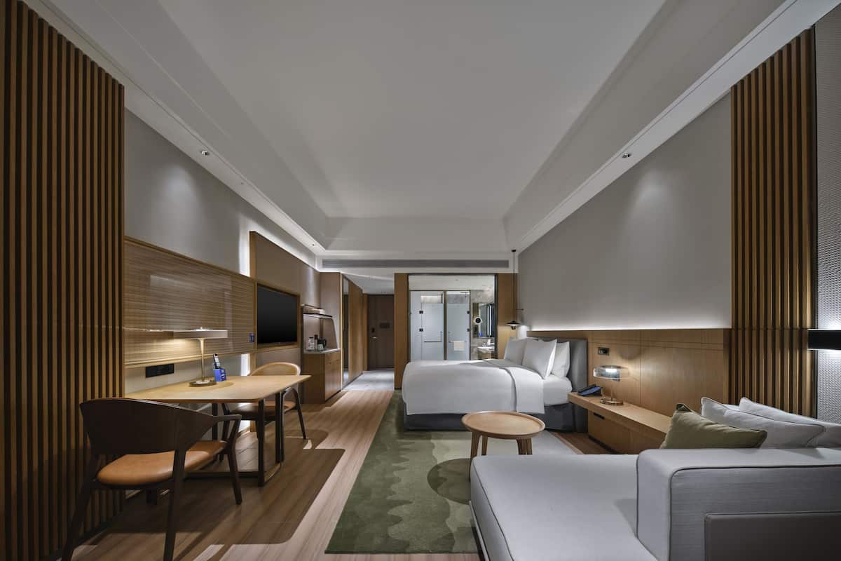 A modern hotel room with a bed, a sofa, a desk, and a chair.
