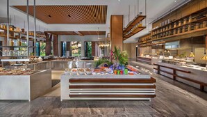 Un moderno vestíbulo de hotel con zona de bar central, techo de madera y grandes ventanales que ofrecen vistas al exterior.