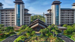 Un hotel con varios pisos, una entrada principal y un jardín ajardinado con palmeras.