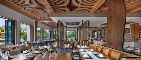 Un restaurante espacioso con techos altos, paneles de madera y grandes ventanales con vistas al exterior.
