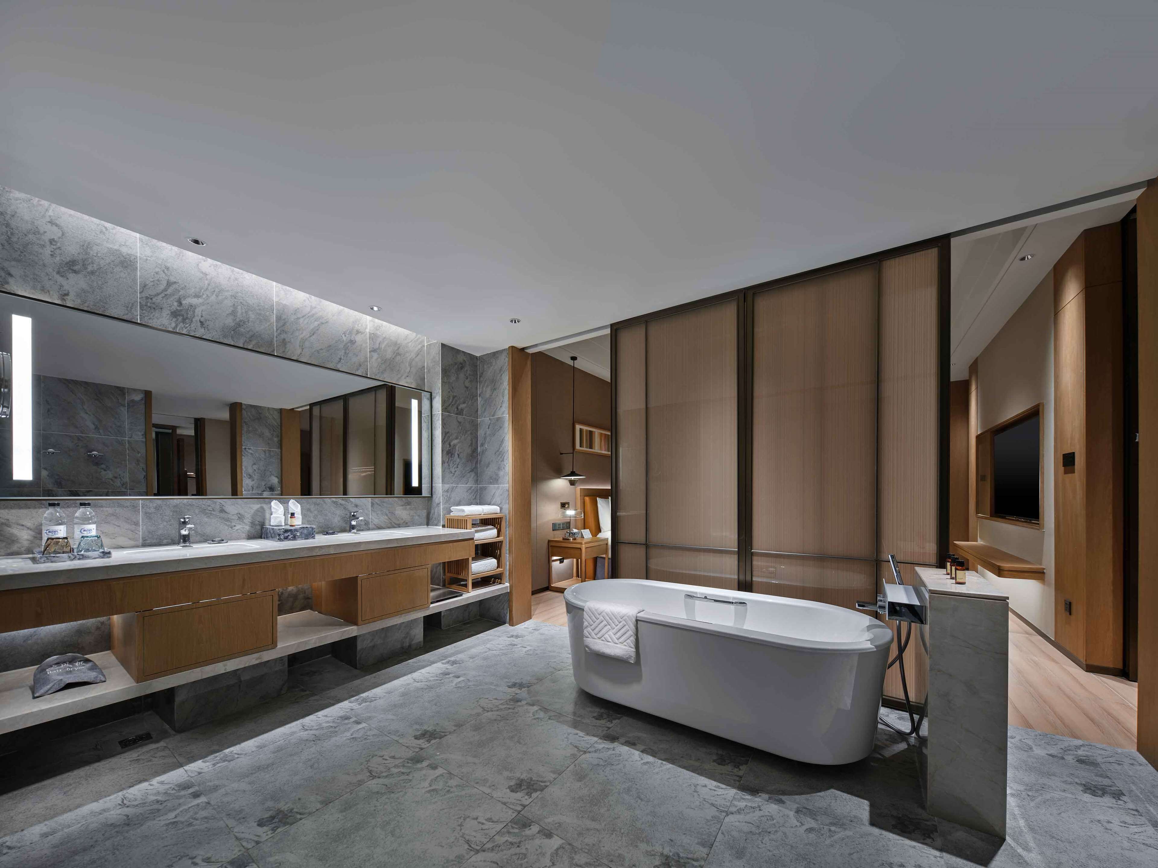 A modern bathroom with a large mirror, two sinks, a bathtub, and wooden cabinetry.