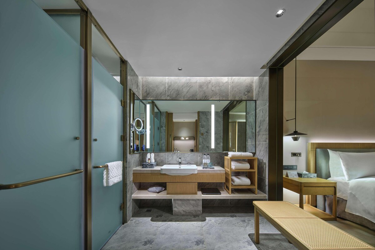 A modern bathroom with a large mirror, a sink, and a bench.