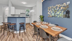 A modern kitchen with white cabinets, a wooden dining table set for six, and a blue accent wall with mirrors. - 2 Bedroom Vacation Condo (2011) (Kissimmee)