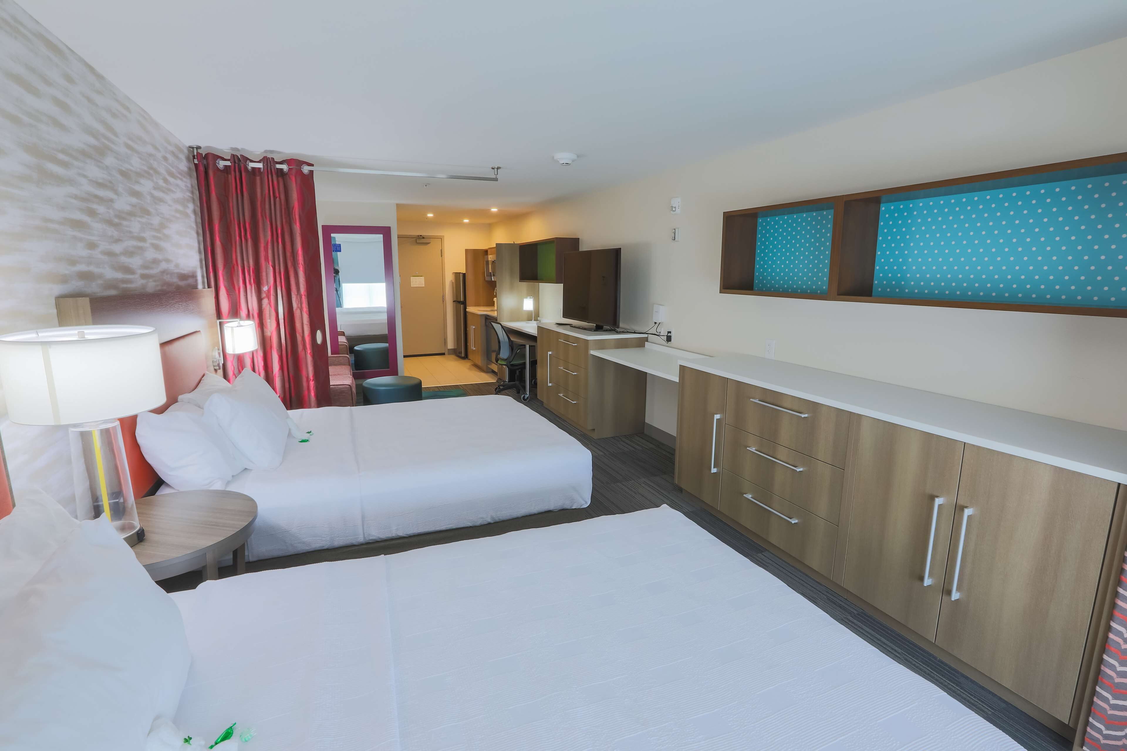Ett hotellrum med två sängar, ett litet skrivbord, ett litet kök och ett badrum som syns i bakgrunden.