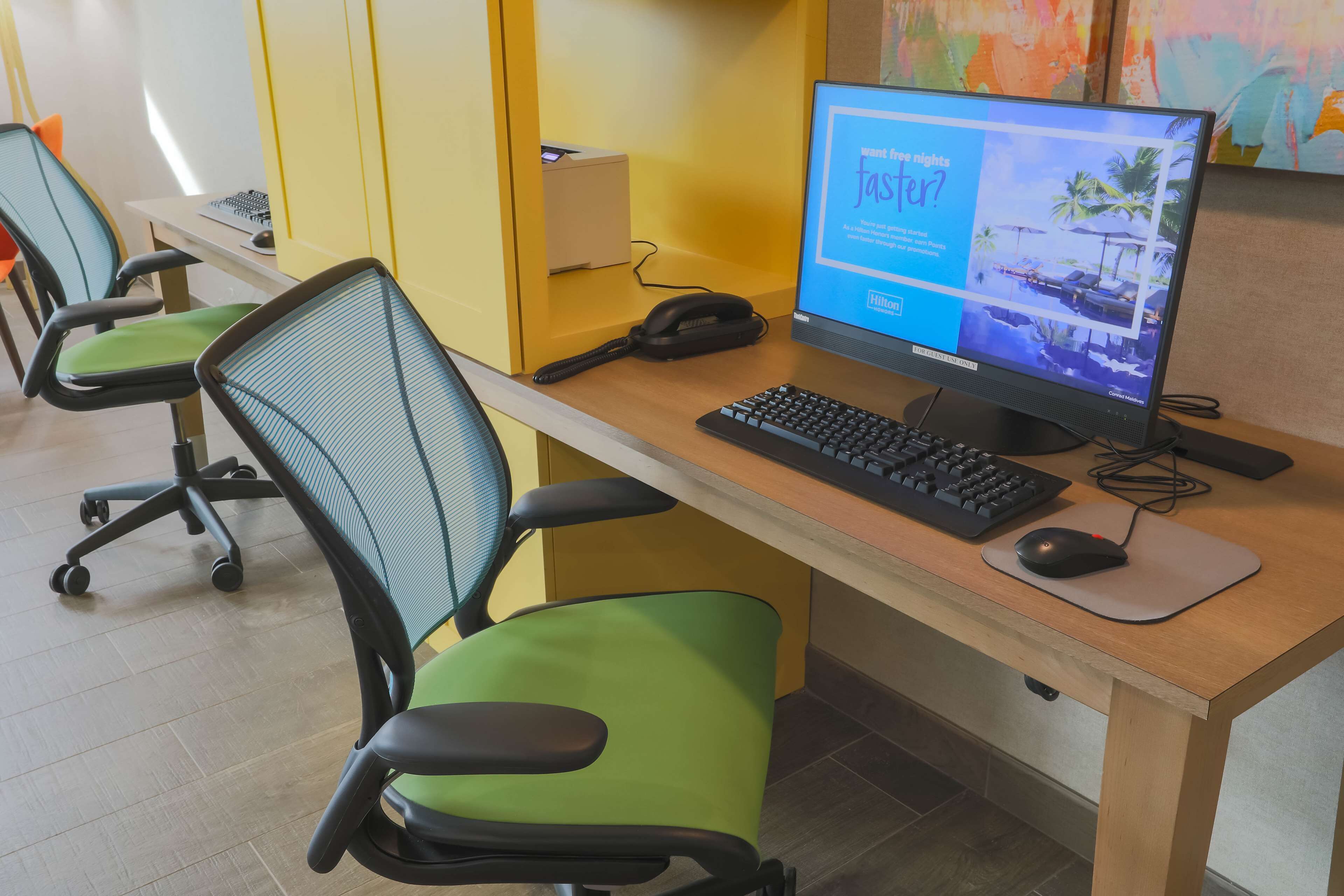 A hotel workspace with a desk, computer, keyboard, mouse, and two office chairs.