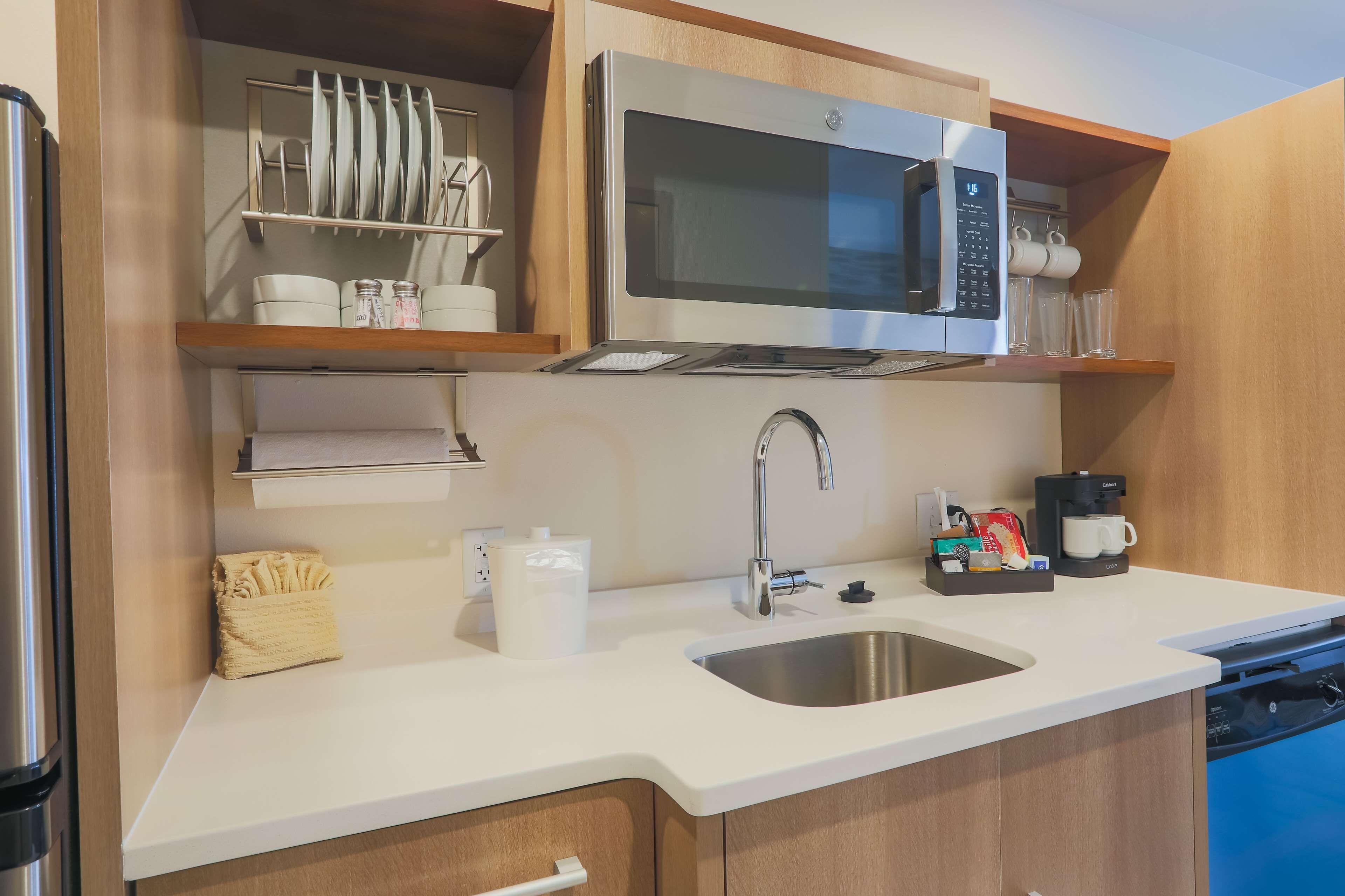 A compact kitchen with a stainless steel microwave, a sink, and a coffee maker.