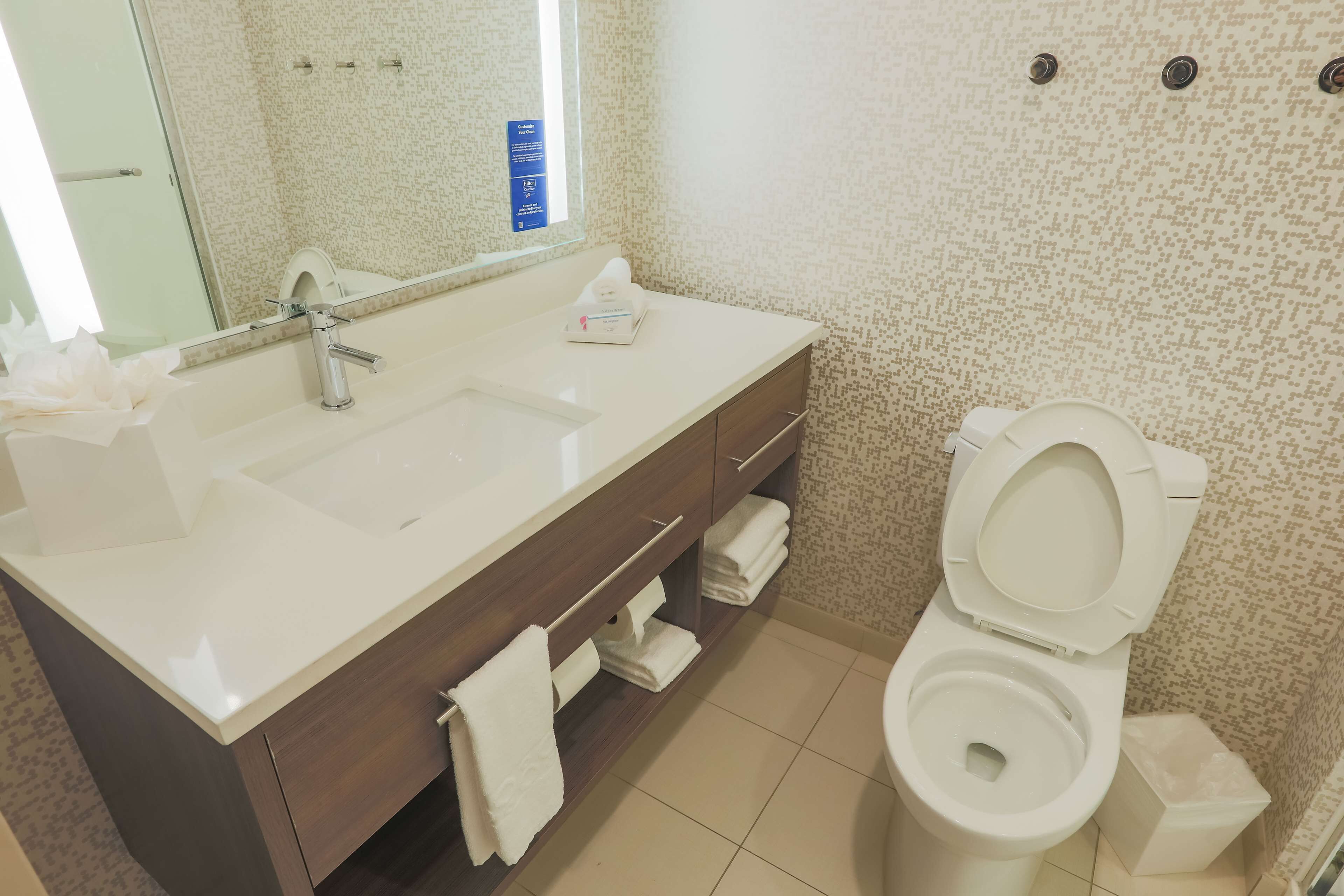 A bathroom with a white sink, mirror, and toilet. There are towels and a tissue box on the sink counter.