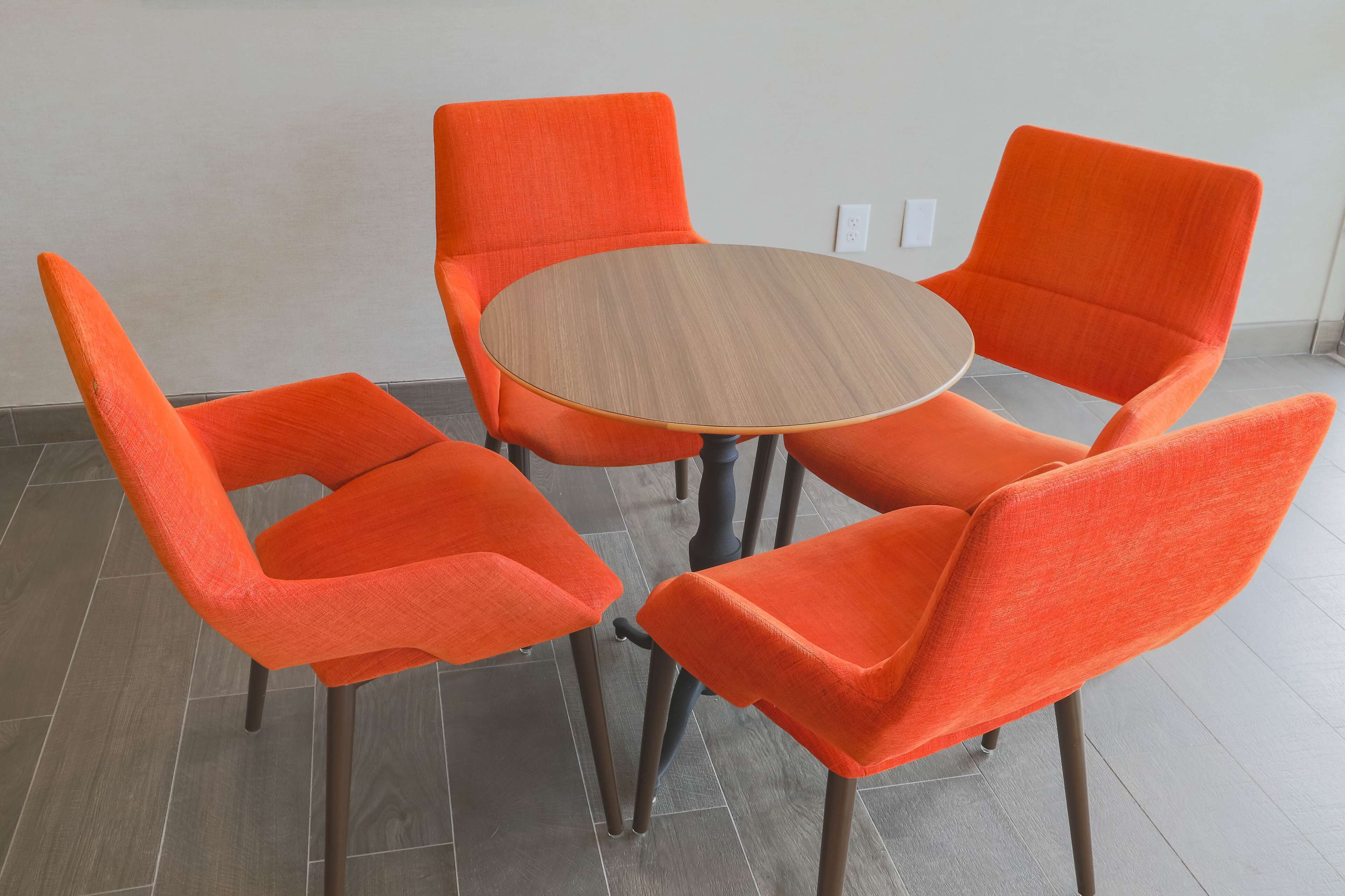 A round wooden table surrounded by four orange chairs with metal legs.