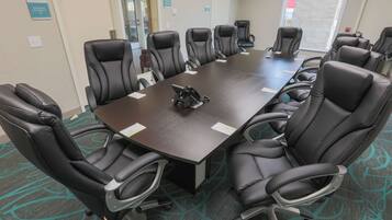 A conference room with a long table and multiple black leather chairs.