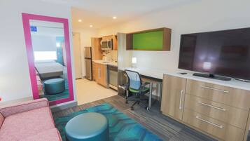 Una habitación de hotel compacta con kitchenette, una cama, un televisor y un rincón de descanso.
