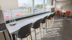 Ein modernes Hotelzimmer mit großem Fenster, einer Bar mit schwarzen Stühlen und Blick auf den Parkplatz.