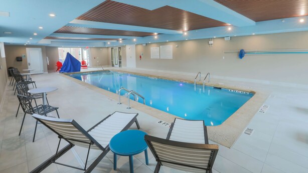 Ein Innenpool mit Liegestühlen und Tischen, eine Decke mit Holzbalken und eine Tür zu einem weiteren Raum.