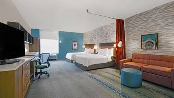 A hotel room with a bed, two bedside tables, a desk with a chair, a television, a sofa, and a patterned rug.