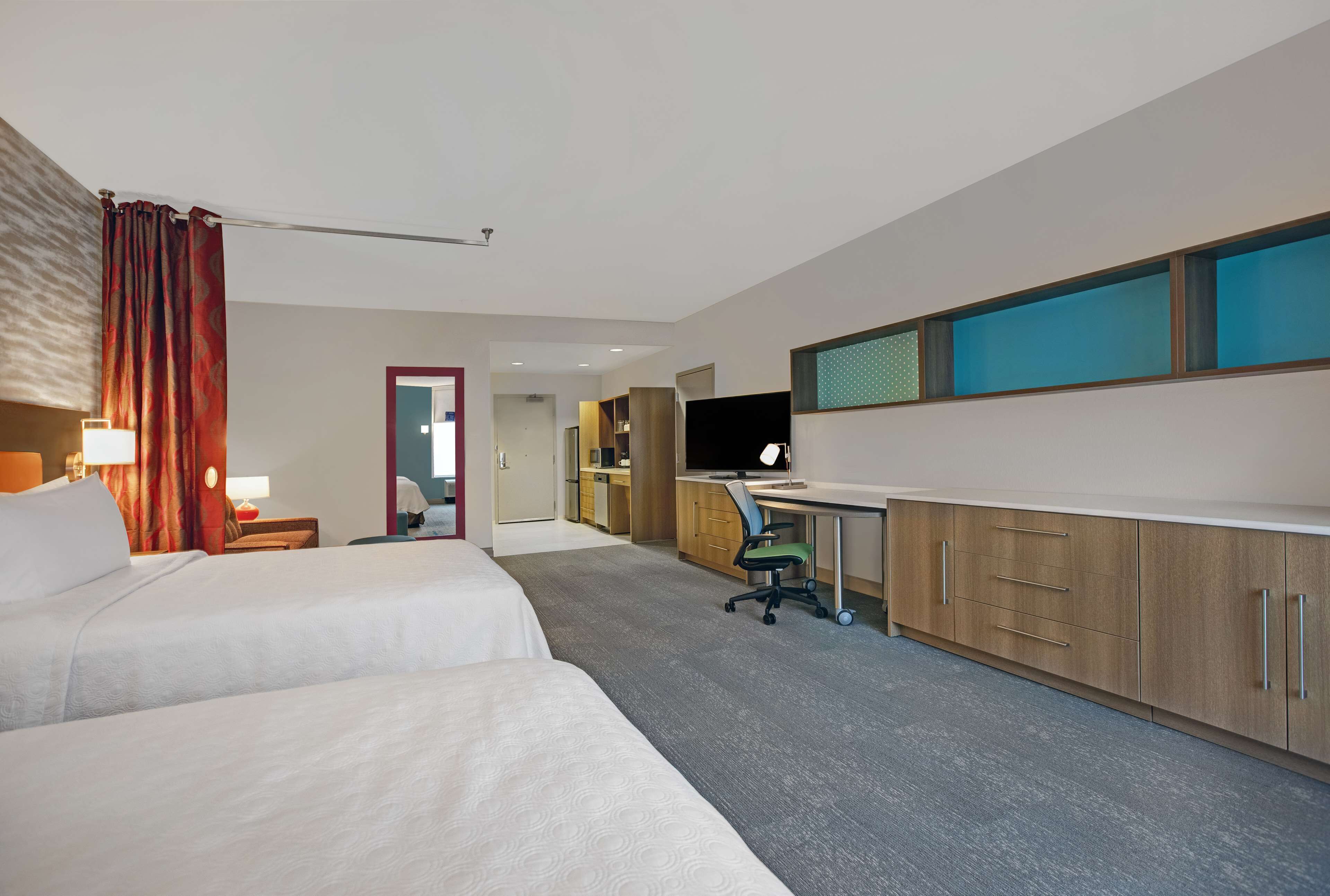Una habitación de hotel con dos camas, un escritorio, una silla, un televisor y un armario.