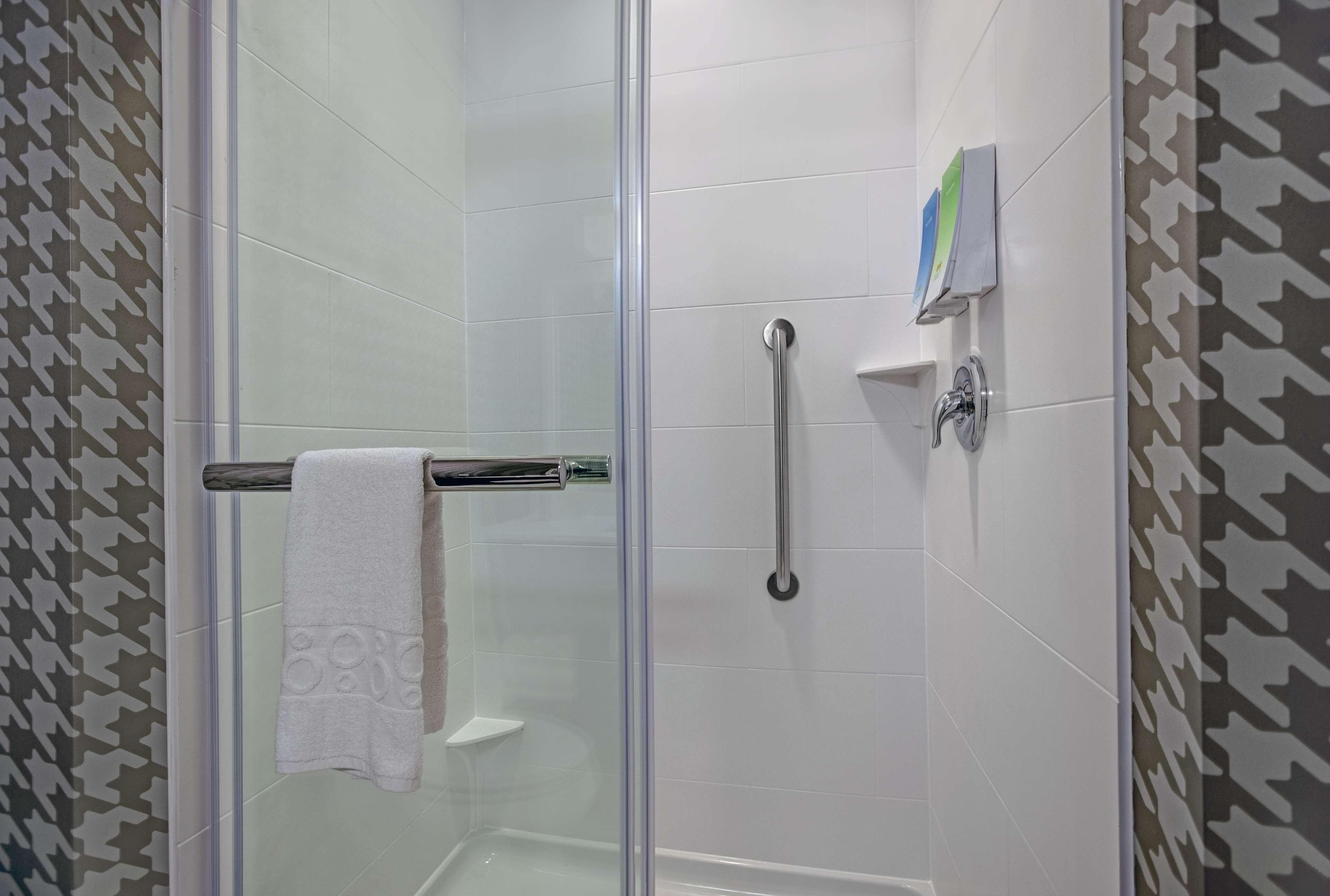 Cabina de bany amb portes de vidre, una tovallola blanca sobre una barra de metall, un vàter de mà i un dispensador de sabó fixat a la paret.