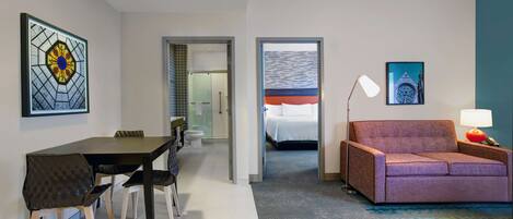 A hotel room with a dining area, a sofa, a bed, and a bathroom visible through an open door.