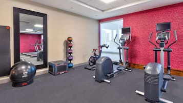 Une salle de sport équipée de matériel d’exercice, avec un miroir et un mur rouge.