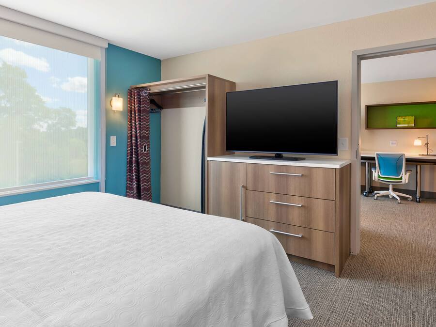 Ein Hotelzimmer mit Bett, Fernseher, Schreibtisch und Stuhl sowie Blick ins Freie.