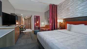 A hotel room with a bed, desk, chair, TV, and a bathroom with a mirror and toilet.
