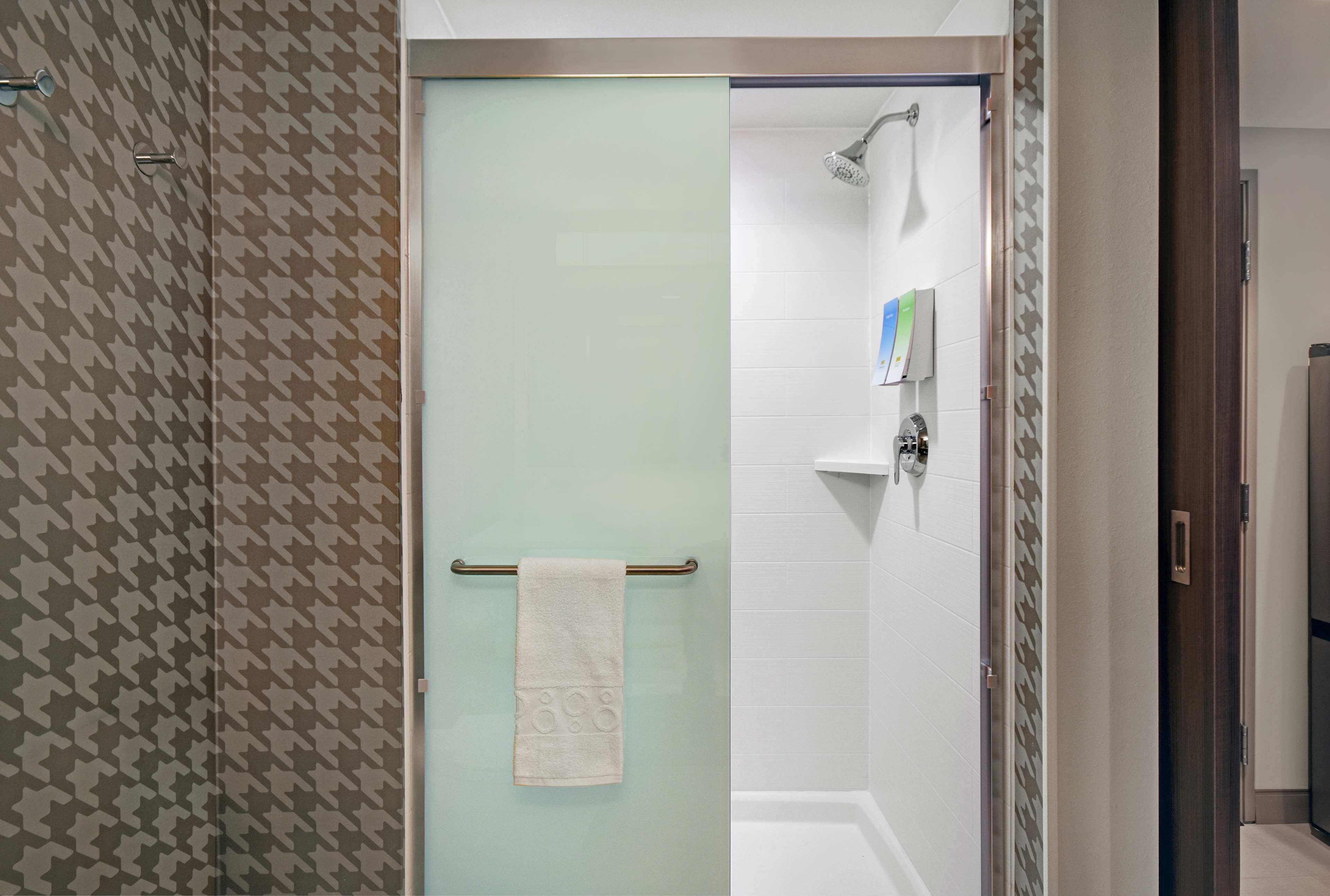 A bathroom with a glass shower door, a towel rack with a towel, and a white tiled wall.