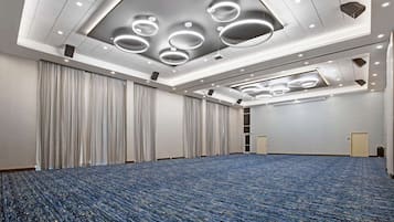 A large conference room with a blue carpet, white walls, and a ceiling with circular light fixtures.