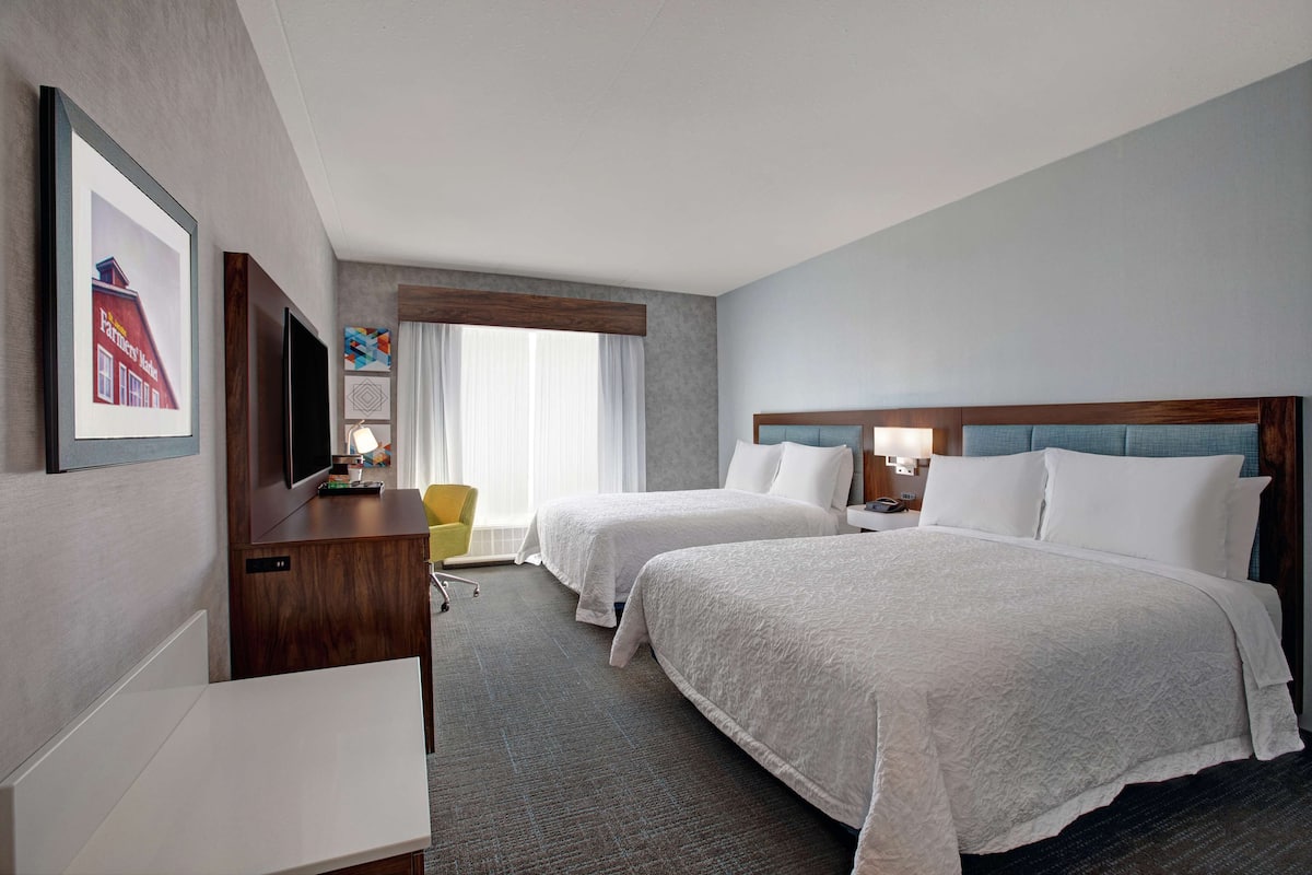 A hotel room with two beds, a desk, a chair, and a TV.