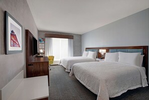 A hotel room with two beds, a desk, a chair, and a TV.