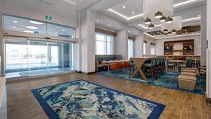 A spacious lobby with a large blue rug, seating areas, and a bar. - Hampton Inn & Suites by Hilton Waterloo St. Jacobs (Township of Woolwich)